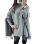 Woman wearing a grey knit poncho sweater with high neckline and fringe tassels, perfect for winter fashion.